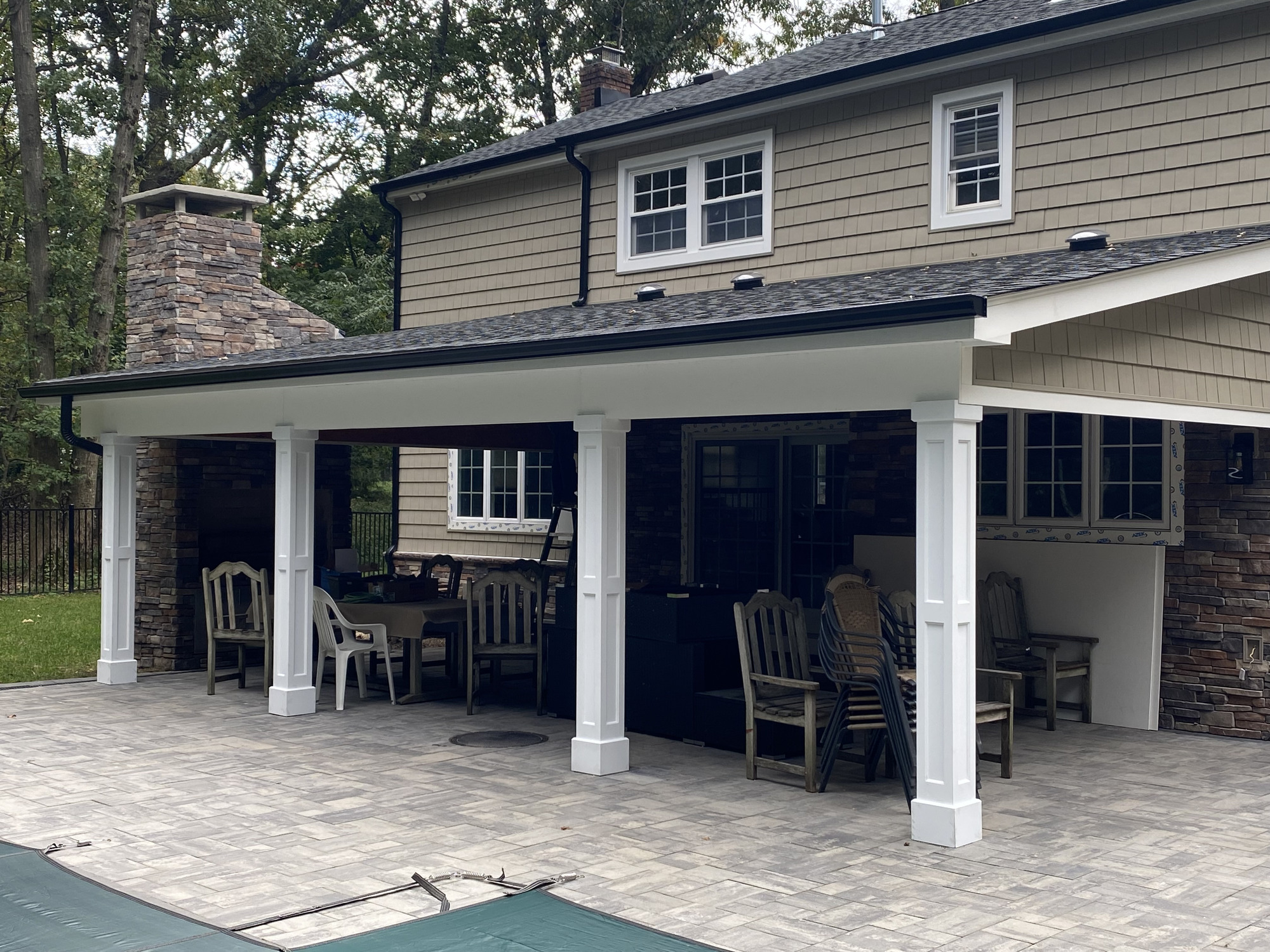 Covered patio with white columns, stone chimney, dark roof, and paved outdoor living surface