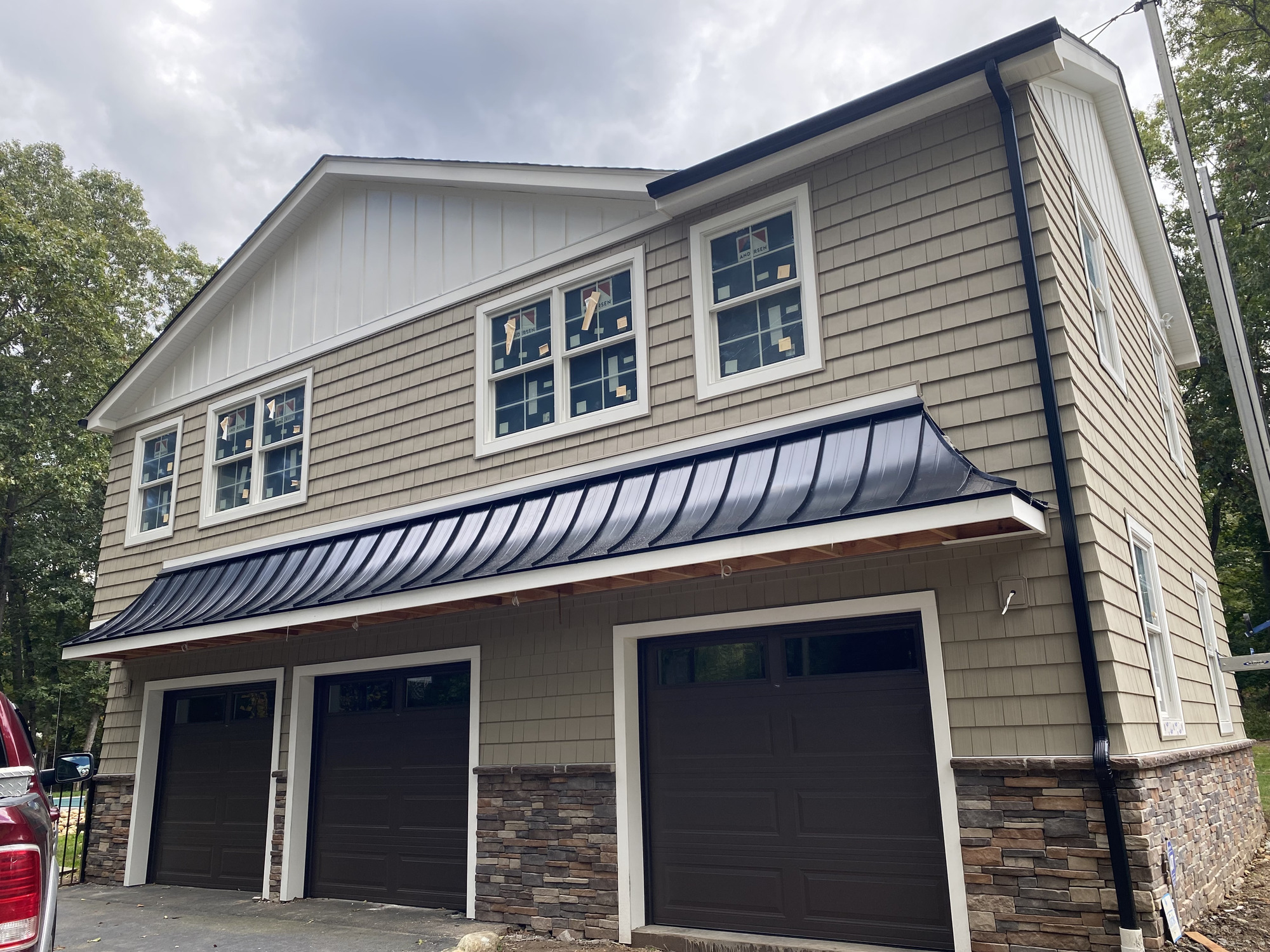 Two-story exterior with shingle-style siding, labeled windows, stone-look base, and dark awning roof during construction