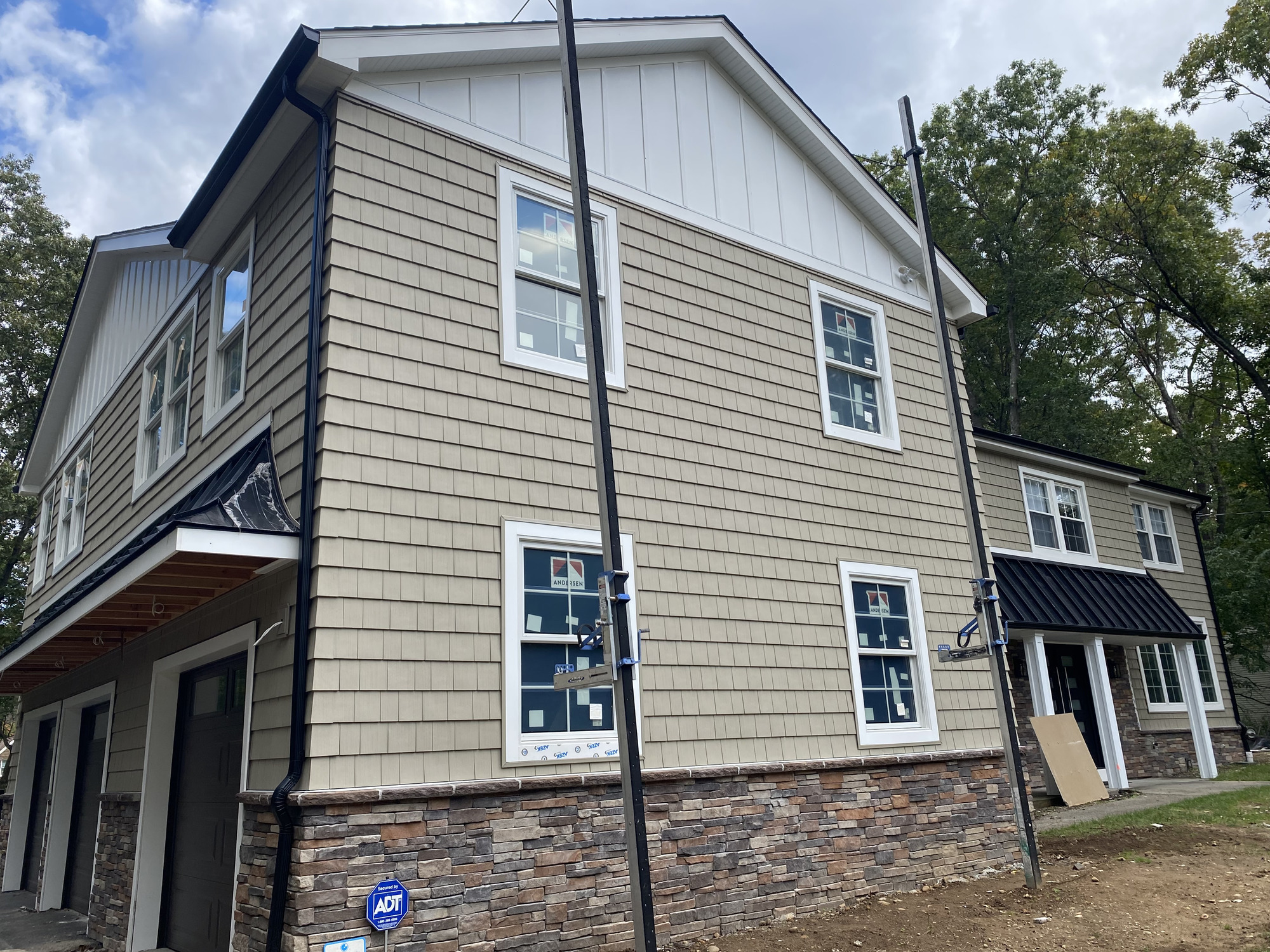 Side elevation during exterior construction with siding, windows, stone-look base, and roof details
