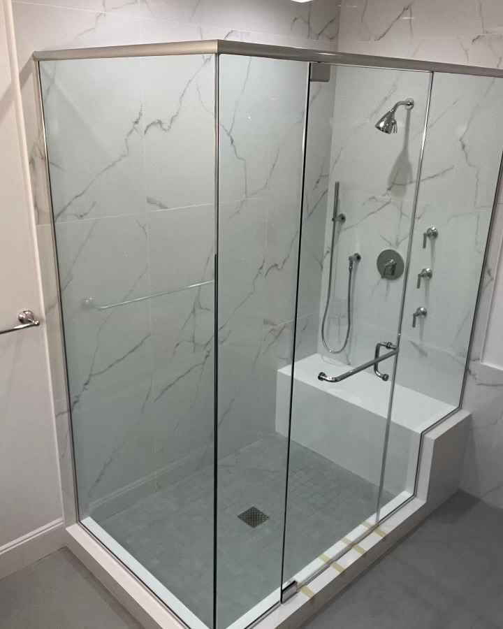 Glass-enclosed marble-look shower with built-in bench, handheld fixture, and grab bars